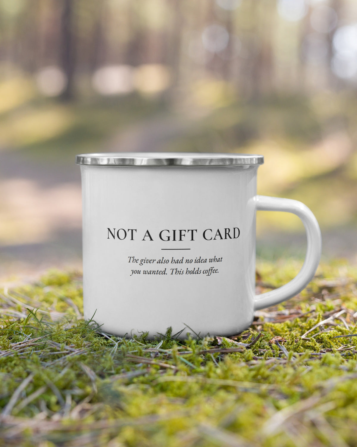 The Not a Gift Card enamel mug on moss in a forest